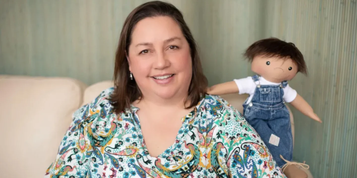 Une petite fille souriante tenant une poupée de l'association A Doll Like Me, personnalisée pour lui ressembler avec son appareil médical.