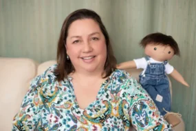 Une petite fille souriante tenant une poupée de l'association A Doll Like Me, personnalisée pour lui ressembler avec son appareil médical.