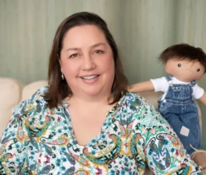 Une petite fille souriante tenant une poupée de l'association A Doll Like Me, personnalisée pour lui ressembler avec son appareil médical.