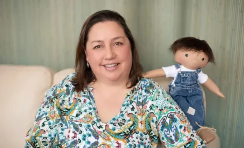 Une petite fille souriante tenant une poupée de l'association A Doll Like Me, personnalisée pour lui ressembler avec son appareil médical.