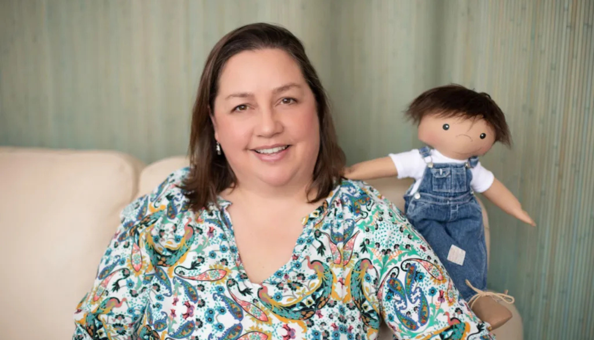 Une petite fille souriante tenant une poupée de l'association A Doll Like Me, personnalisée pour lui ressembler avec son appareil médical.