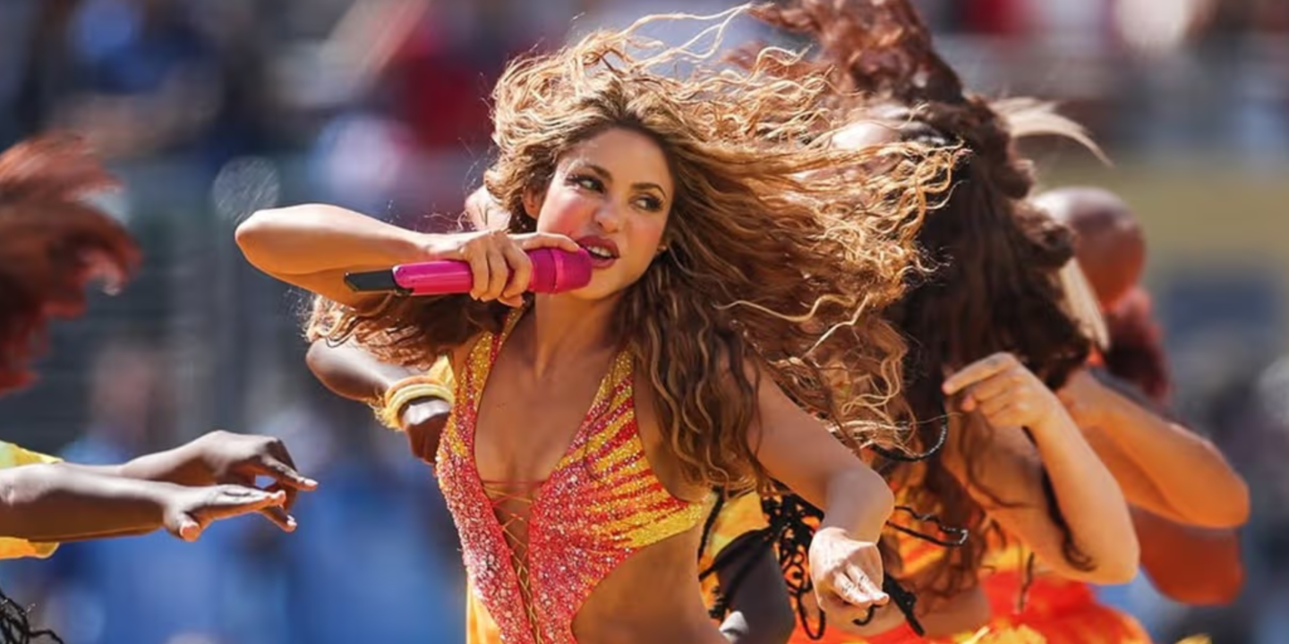 Shakira chantant au micro sur scène, éclairée par des lumières orangées lors d'un concert