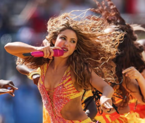 Shakira chantant au micro sur scène, éclairée par des lumières orangées lors d'un concert