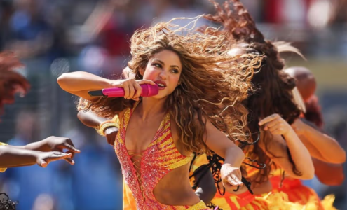 Shakira chantant au micro sur scène, éclairée par des lumières orangées lors d'un concert